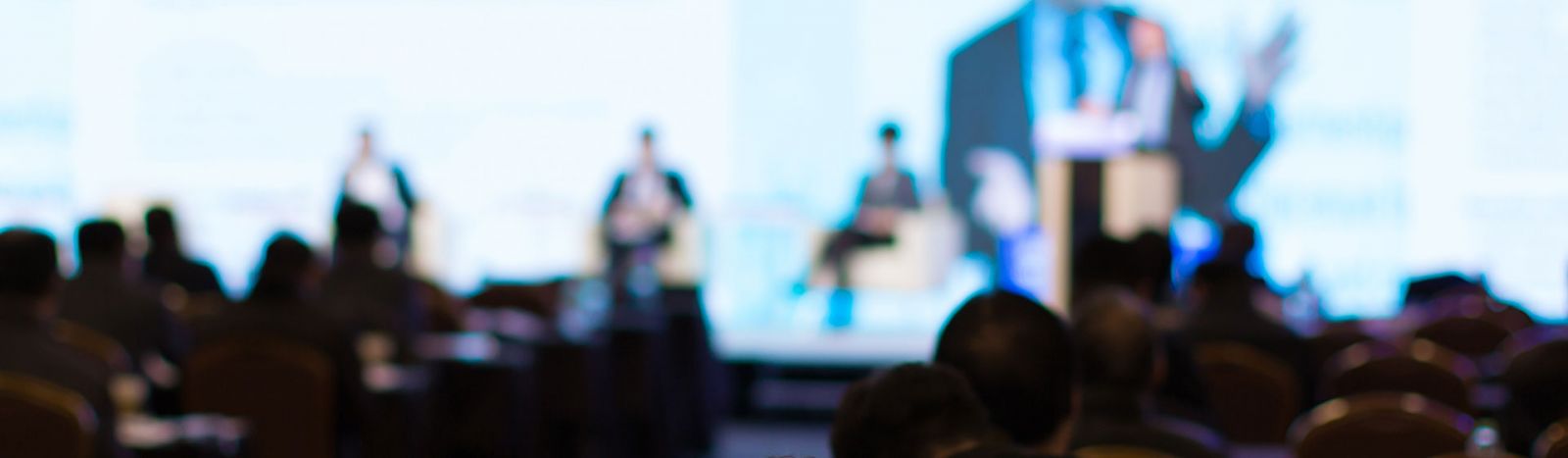 Blurred image of presenters on stage at a conference banner image